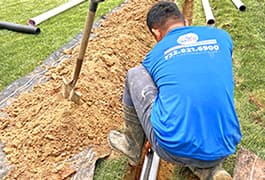 An employee from Middlesex Gutters digs a trench as part of an underground gutter system installation, wearing protective gear and using a shovel to ensure proper drainage.